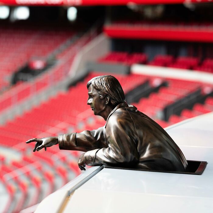 Bronze street art sculpture by Frankey creatively interacting with public space in a stadium setting.