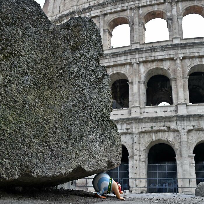 Street art interpretation of public spaces showing a cartoon figure pushing a giant stone near the Colosseum.