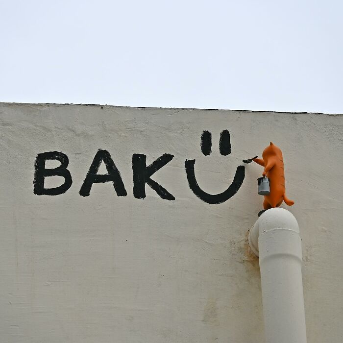 Street art interpretation of public spaces showing a small orange figure painting a smiley on an urban wall.