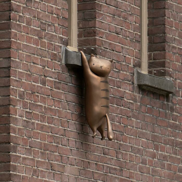 Bronze cat sculpture cleverly integrated into public space on a brick building as street art by Frankey.
