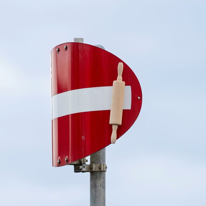 Street art on a no entry sign creatively transformed with a wooden rolling pin on a metal pole outdoors.