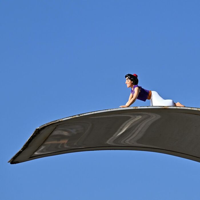 Miniature figure of a character crawling on a curved metal surface showcasing clever street art in public spaces by Frankey.