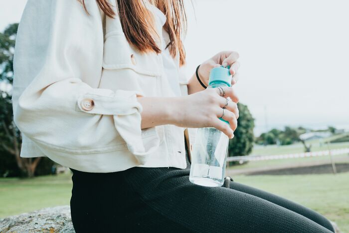 Person in casual clothes opening a water bottle outdoors, illustrating ingenious inventions that found new purposes over the years.