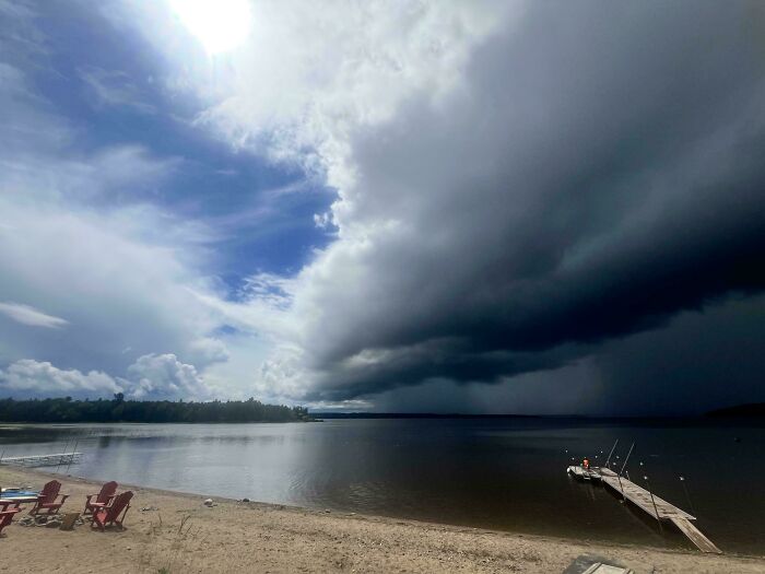 Dark storm clouds over a lakeshore with a dock and chairs, showcasing wild mother nature acting on its own terms.