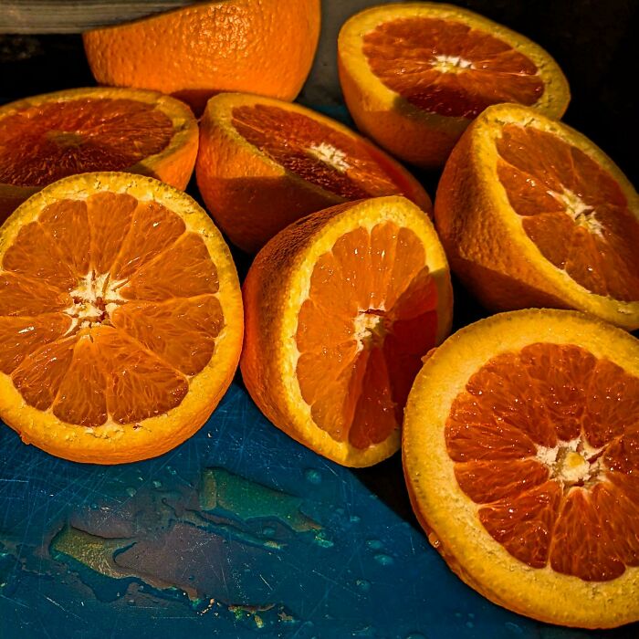 Close-up of vibrant orange slices arranged on a blue surface, capturing accidental renaissance photo lighting and texture.