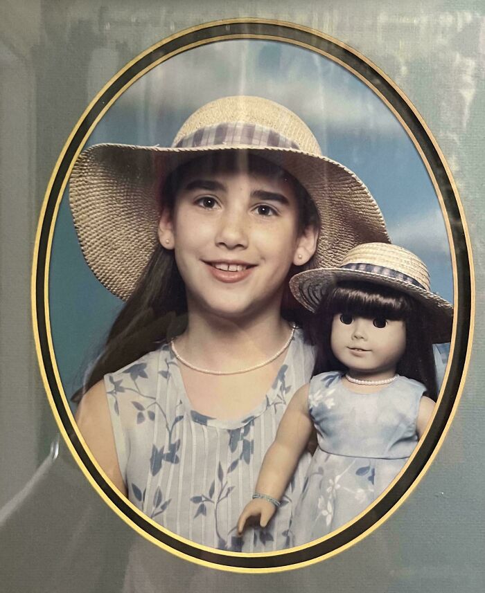 Young girl and doll wearing matching hats and dresses in a framed photo from people’s regrettable past collection.