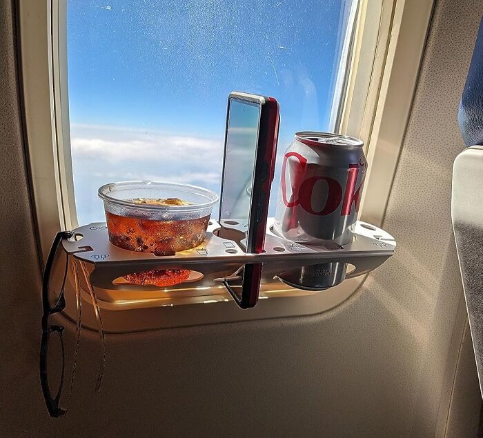 Airplane window tray organizer holding snacks, a drink, and a phone, perfect for hassle-free travel essentials.