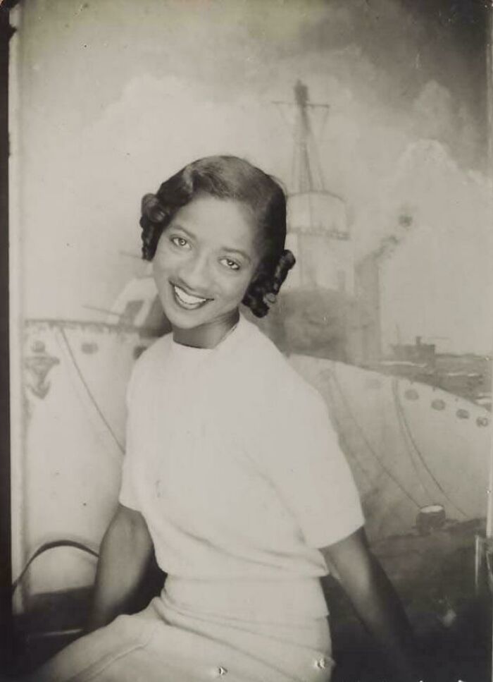 Vintage photo of a smiling woman posing in front of a painted ship backdrop, showcasing candid glimpses into the past.
