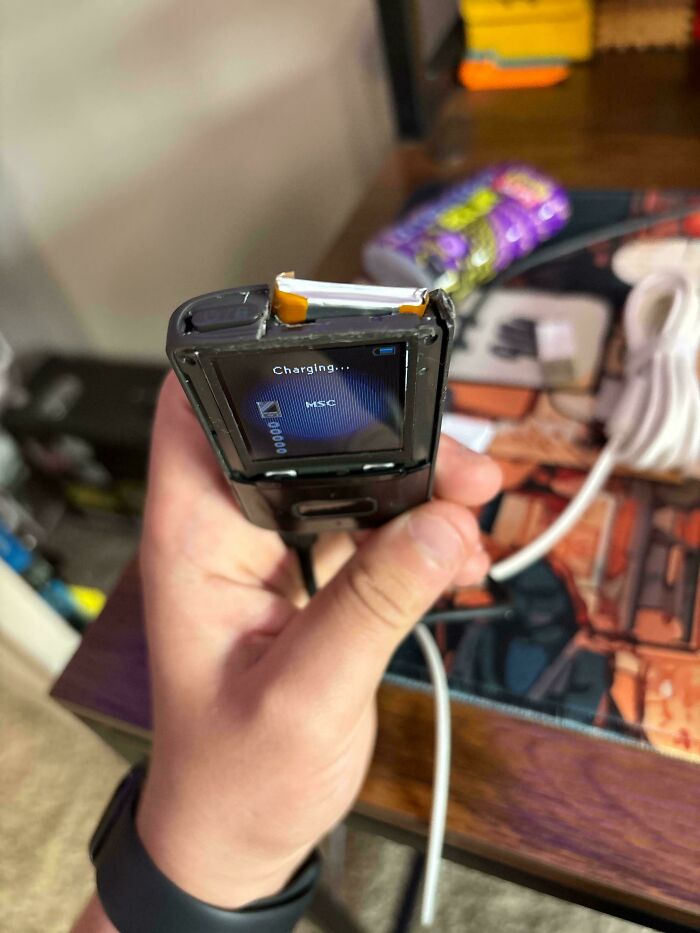 Hand holding a broken device with a damaged screen showing charging status, illustrating tech support struggles.