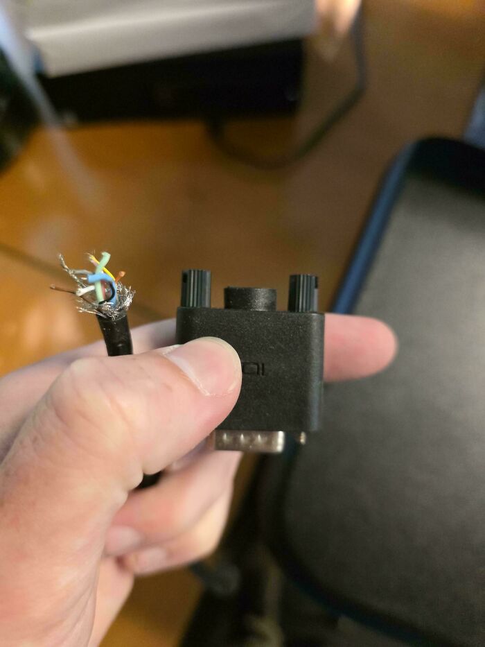 Hand holding a broken tech support cable with exposed wires, illustrating tech support worker frustrations and challenges.