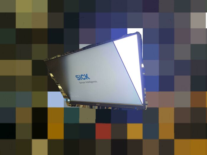 SICK sensor intelligence device mounted against a multicolored pixelated background in a tech support environment.