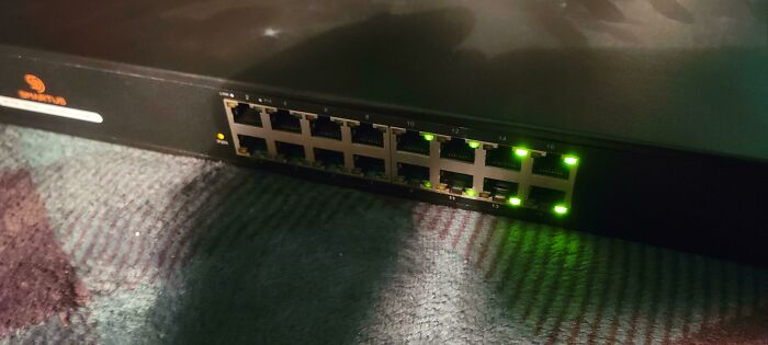 Network switch with active port lights on a carpeted floor, illustrating common tech support worker equipment.