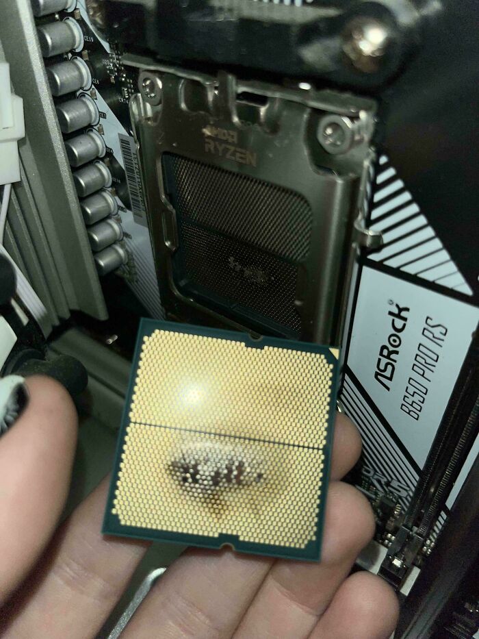 Close-up of a damaged computer processor held by a tech support worker inside a PC with ASRock motherboard visible.