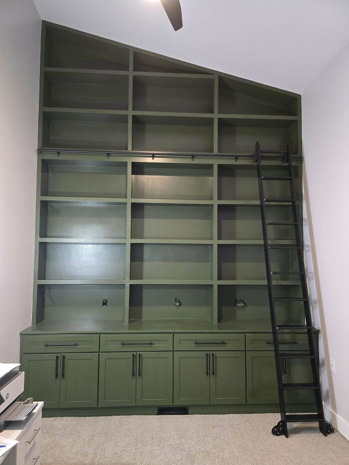 Tall green wooden bookshelf with built-in cabinets and a sliding ladder showcasing woodworking craftsmanship and design.