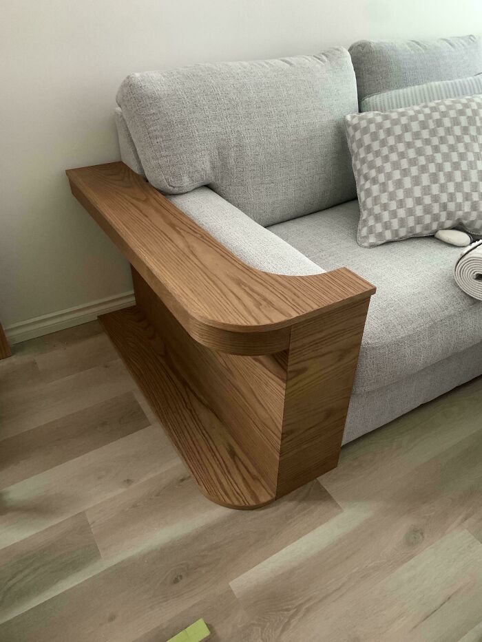 Custom wooden armrest and side table carved and integrated into a modern gray sofa as a woodworking project.