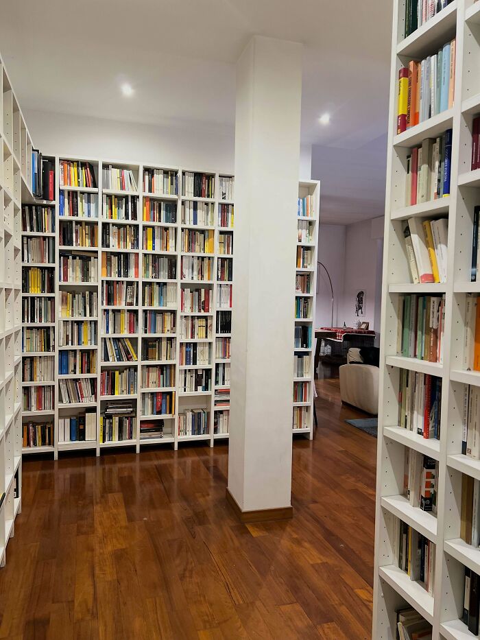 Spacious living space with beautifully decorated home library featuring white shelves and wooden flooring.