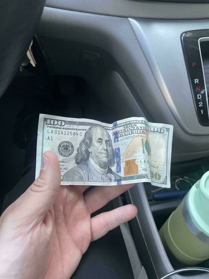 Hand holding a hundred dollar bill found as a dumpster diving treasure inside a car near the gear shift.