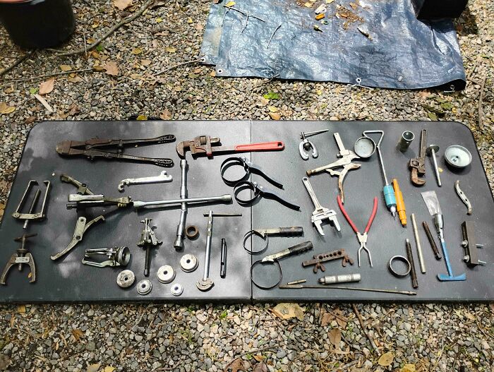 Various vintage tools and mechanical parts laid out on a black table, showcasing dumpster diving treasures collection.