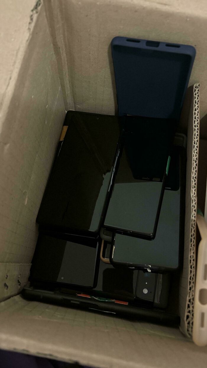 Several smartphones and phone cases stacked inside a cardboard box, a potential dumpster diving treasure.