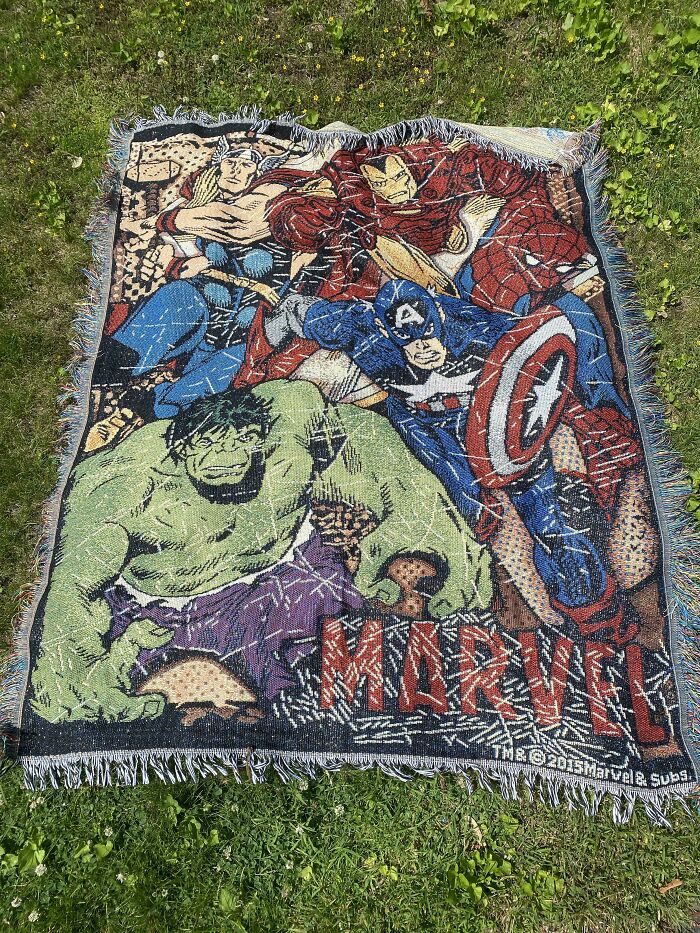 Marvel-themed blanket featuring popular superheroes laid out on grass, a unique dumpster diving treasure find.