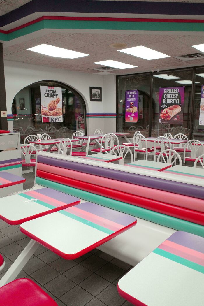 Empty fast food restaurant interior with colorful retro seating and promotional food posters on windows, moderately interesting scene