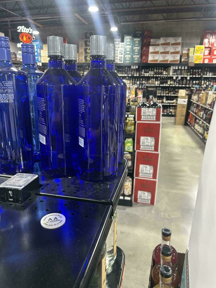 Blue glass bottles on a store shelf with various liquor bottles and boxes in the background, moderately interesting display.
