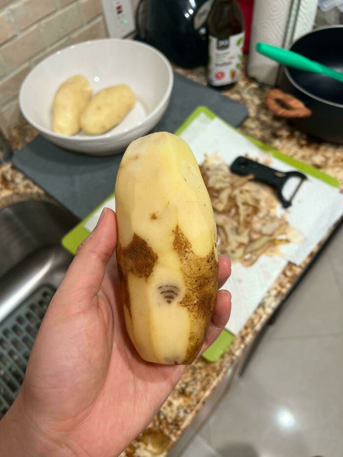 Hand holding a peeled potato with unusual brown markings, one resembling a Wi-Fi symbol, moderately interesting sight.