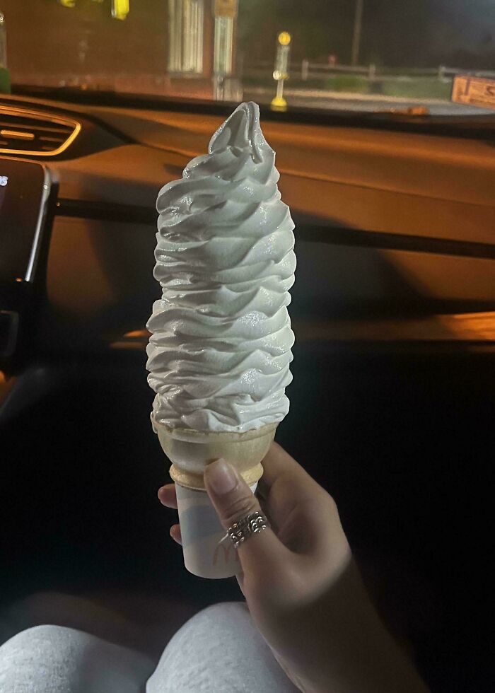 Hand holding an unusually tall ice cream cone inside a car, showcasing a moderately interesting food moment shared.