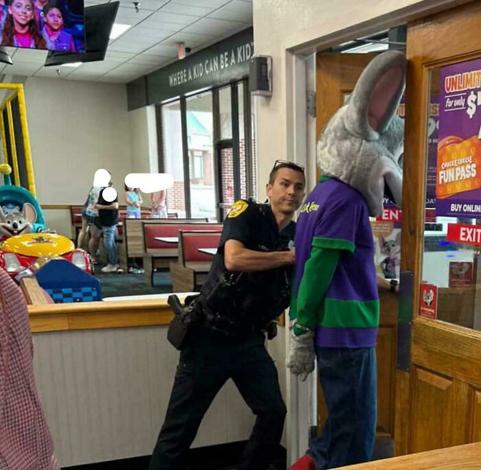 Police officer handcuffing person in a Chuck E. Cheese costume, a moderately interesting moment shared by people.
