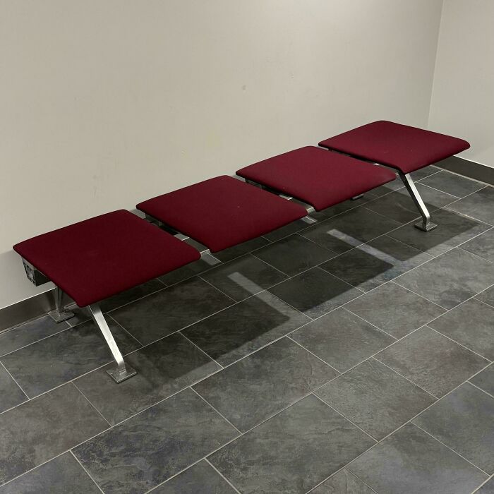 Minimalist bench with four maroon cushioned seats and metal legs on tiled floor in a simple room, moderately interesting design.