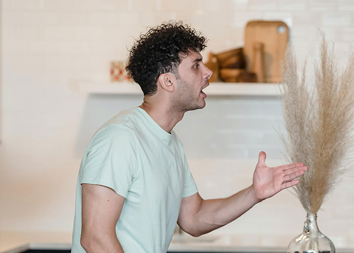Man with curly hair in a light green shirt arguing passionately indoors, illustrating worst cheating stories conflict.