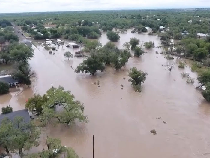 Aerial view of flooded area showing submerged trees and houses, related to Camp Mystic counselor heartbreaking moment.