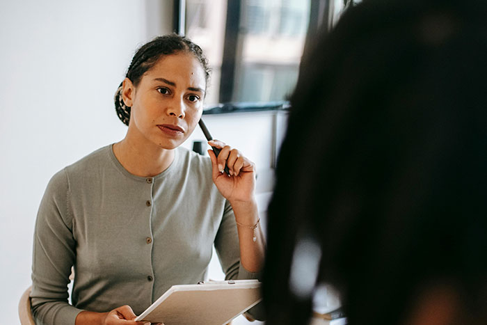Woman holding clipboard and pen, thoughtfully listening during a discussion about big burly men and microfeminisms.