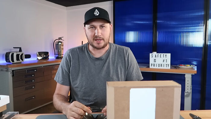 A man sharing insights about unsubscribed YouTubers while sitting at a desk with a cardboard box and tech gadgets.
