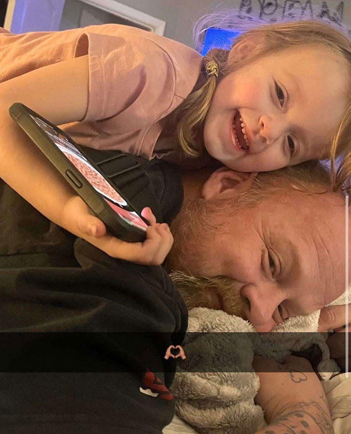 Young girl smiling and holding phone while lying on a man's back, illustrating story about girl finding parents' bodies at home.