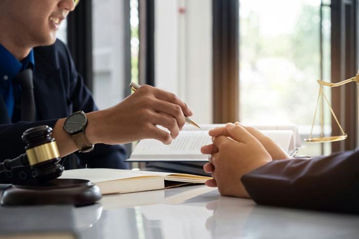 Two women discussing financial documents with legal books and a judge's gavel on a desk in a professional setting.