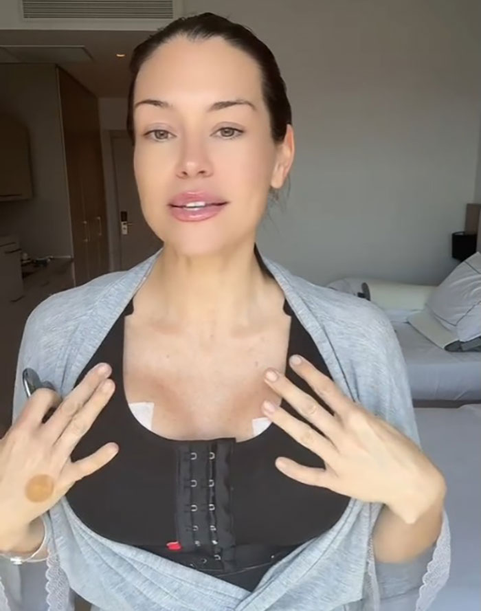 Woman with 3 kids demonstrating recovery after a mommy makeover, showcasing stunning results in casual indoor setting.