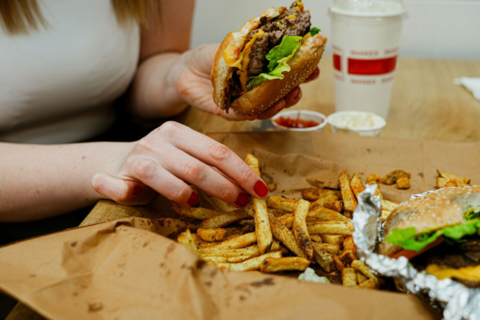 Person holding a cheeseburger and grabbing fries, illustrating the obesity trend in Americans and unhealthy eating habits. - 7