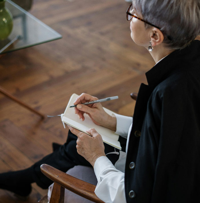 Therapist in glasses writing notes in a notebook during a session about differences between men and women. - 11