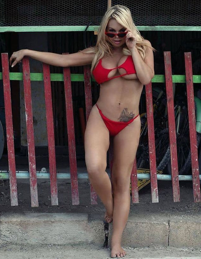 Woman in a red bikini posing by a red wooden fence, highlighting adult industry mental health substance-related issues.