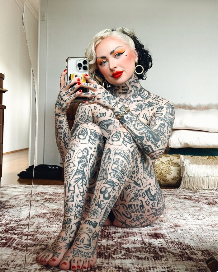 Woman with extensive tattoos covering her body suit transformation taking a selfie, showing bold makeup and earrings. - 8