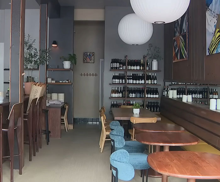Cozy restaurant interior with wooden tables, chairs, wine bottles on shelves, and modern hanging white lamps.