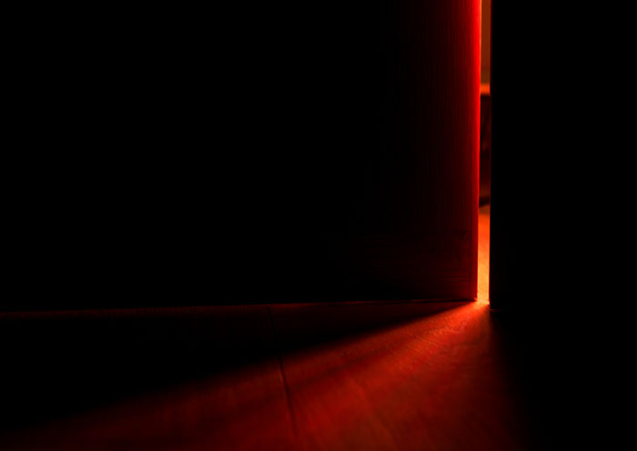 Dimly lit partially open door casting eerie red light on floor, evoking real-life horror stories and unexplainable encounters. - 6
