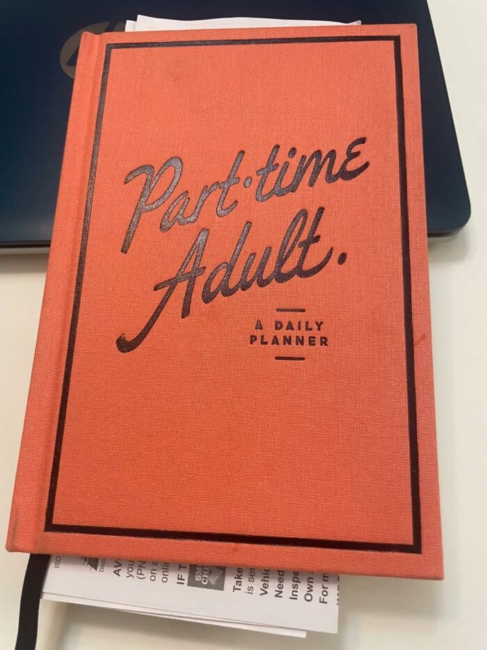 Orange daily planner titled Part-time Adult resting on papers and a laptop, a cool item to covet for peak coolness enthusiasts.