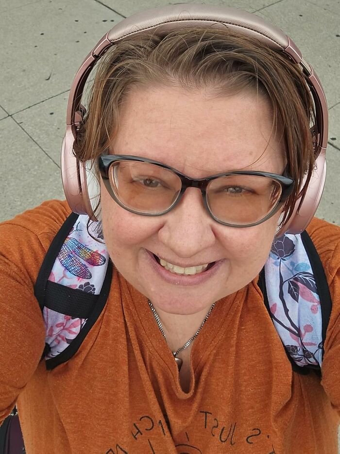 Smiling woman wearing headphones and glasses, carrying a floral backpack, ready to ditch travel drama with expert-approved finds.