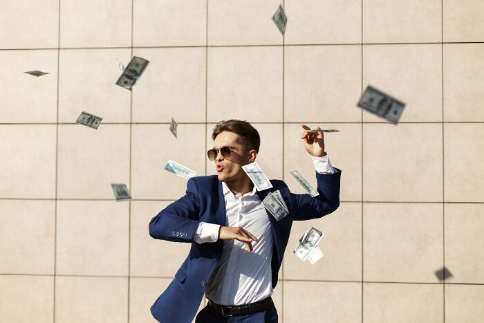 Young man in sunglasses throwing money in the air, illustrating trends leading to overconsumption and excessive spending. - 7