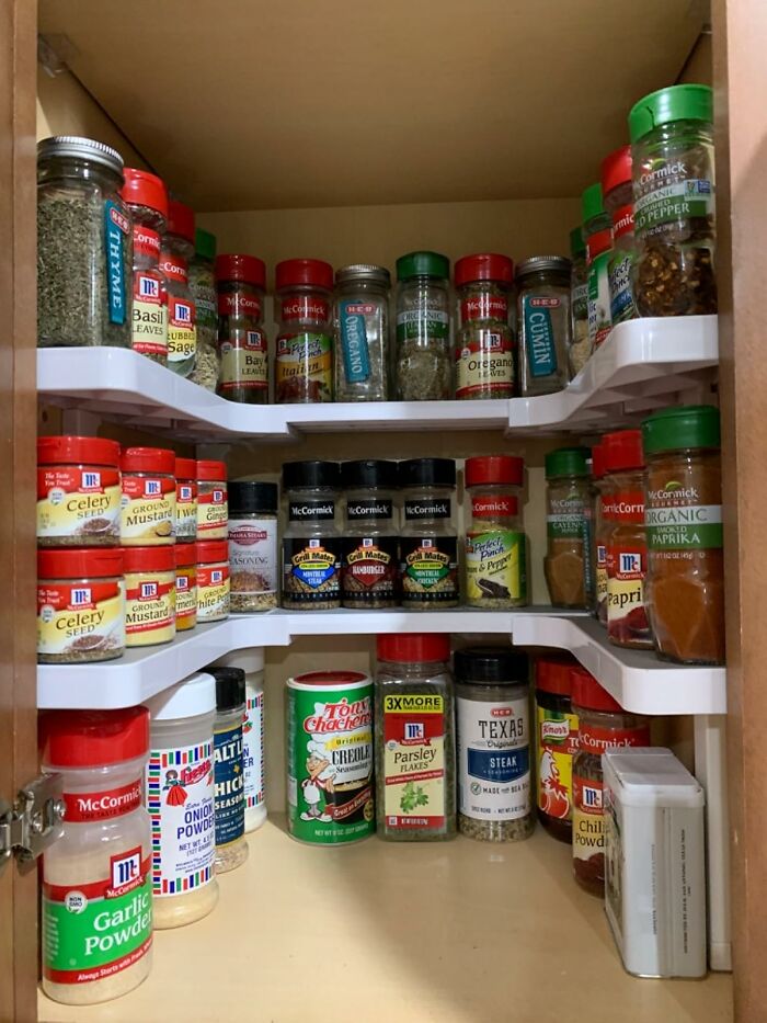 Organized spice rack inside kitchen cabinet using shelf organizers to hide ugly clutter and maximize space in home.
