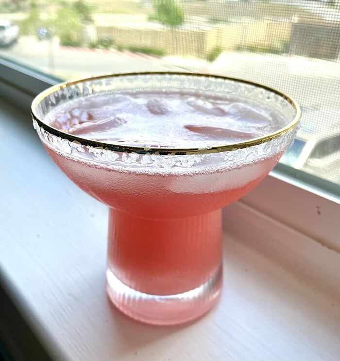 Pink cocktail with a salted gold rim served in a quirky glass on a windowsill, perfect for quirky finds lovers.