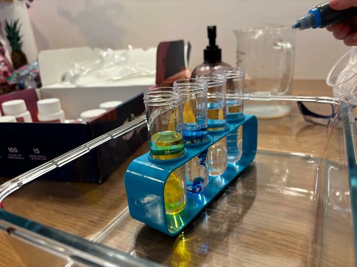 Test tubes with colorful liquids in a blue rack being filled by hand, showcasing a fun hobby for skill time activities.