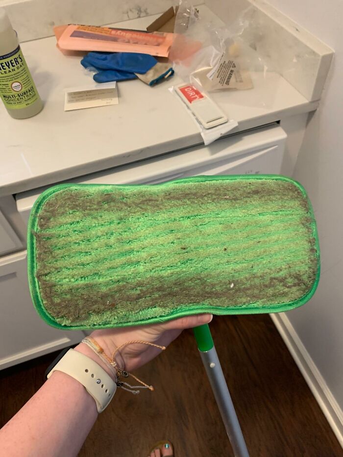 Green microfiber mop head covered in dirt being held in a room, illustrating messy roommate cleanup issues and solutions.